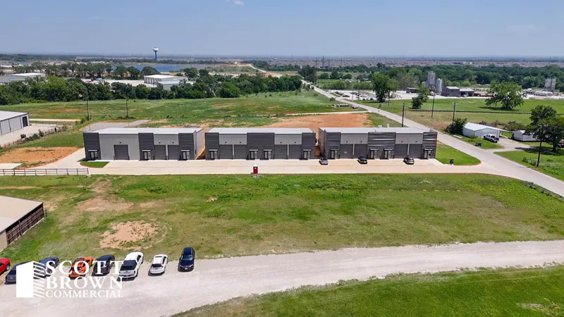 Aerial view of a single-storey terrace of flex units at Fusion Business Park, seen across open grassland, with the town of Aubrey and a water tower in the distance.