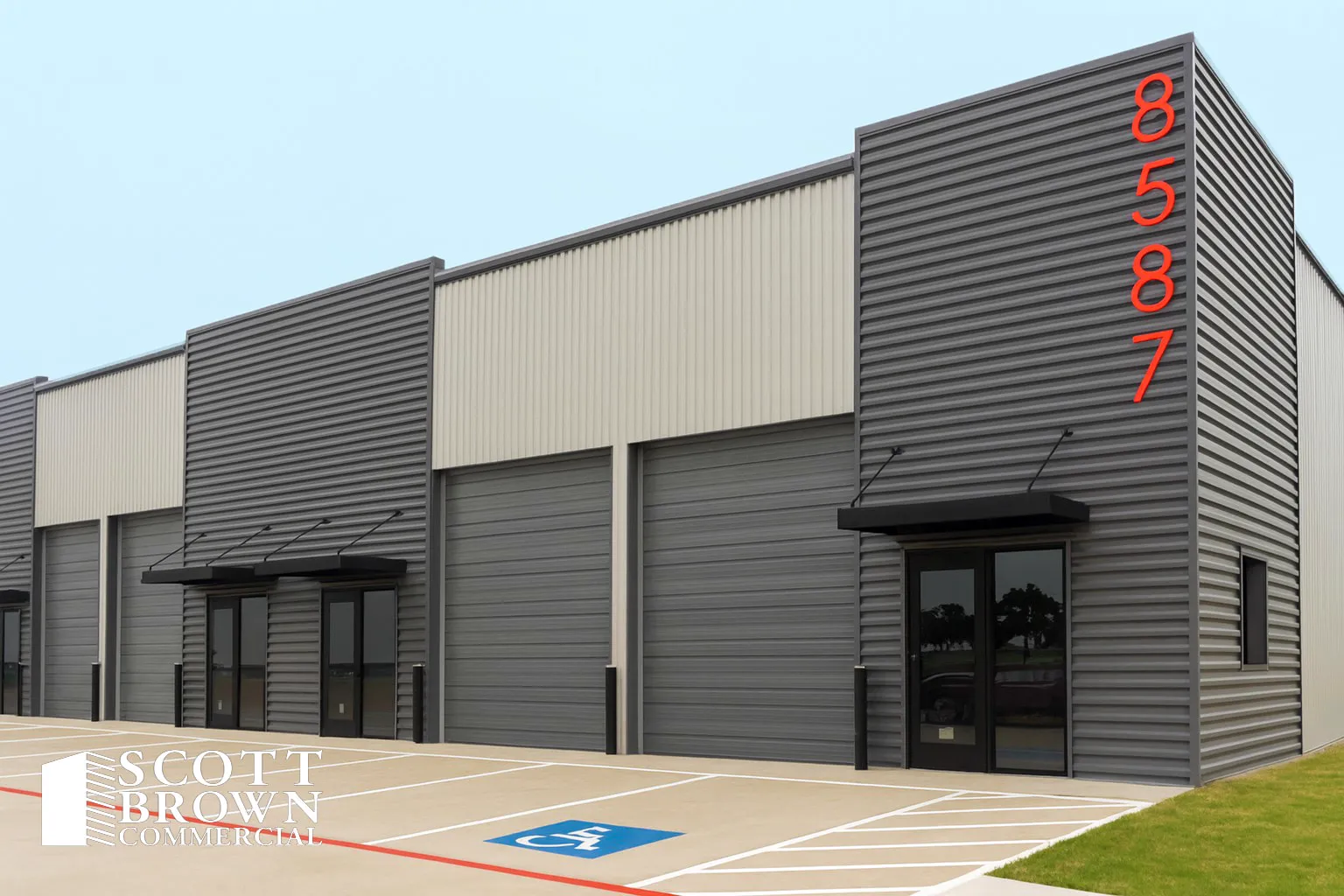 Corner of a Fusion Business Park building: dark profiled metal cladding carrying the address number 8587 painted in orange, two grade-level overhead doors, and a glazed office entrance under a black awning.