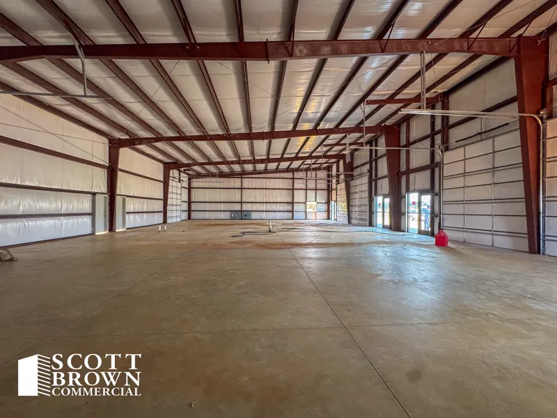 Interior of an empty warehouse bay at Fusion Business Park: clear-span red steel portal frames, white insulated metal wall lining, a sealed concrete floor, and a glazed entrance at the far end.