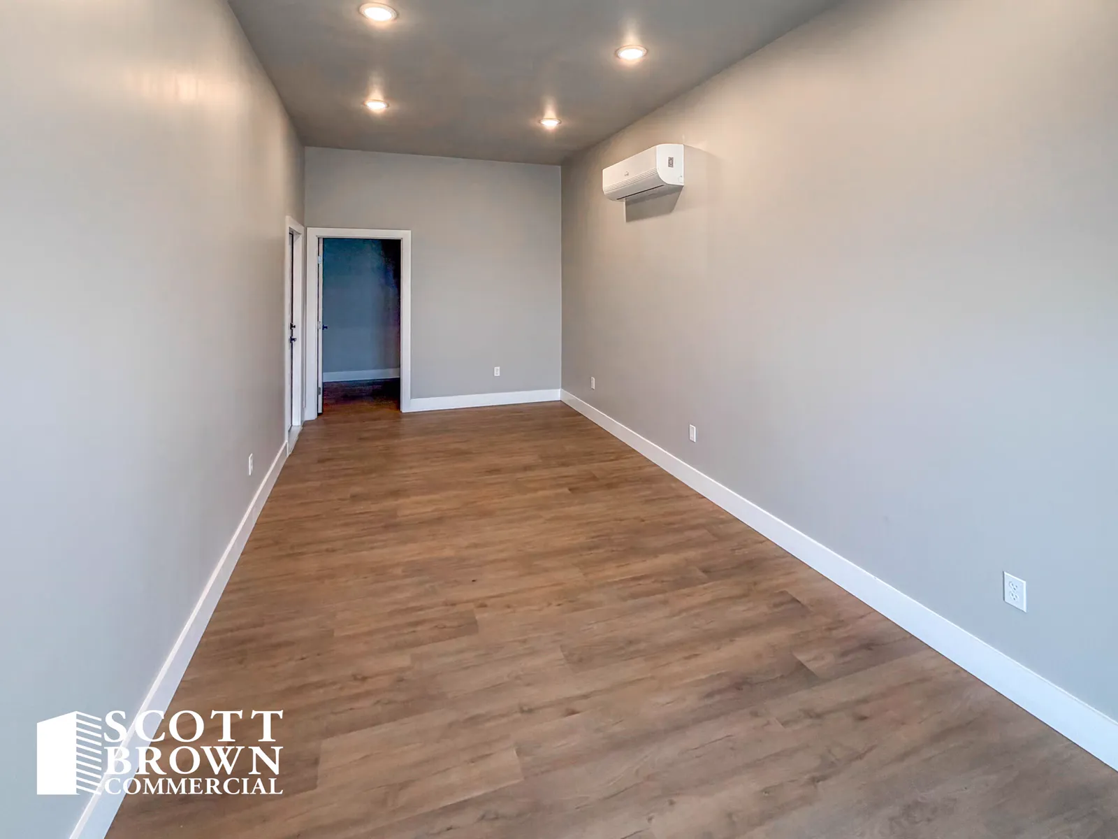 A finished office inside a Fusion Business Park suite: grey painted walls, wood-effect vinyl plank flooring, recessed downlights, and a wall-mounted air conditioning head.