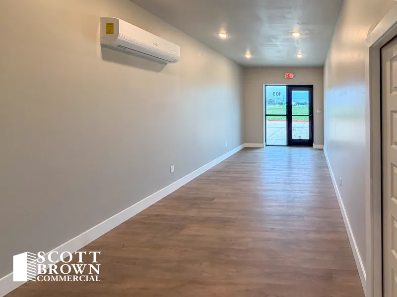 A finished office looking toward the glazed front entrance of suite 103, with wood-effect plank flooring, grey walls, and a wall-mounted air conditioning head.