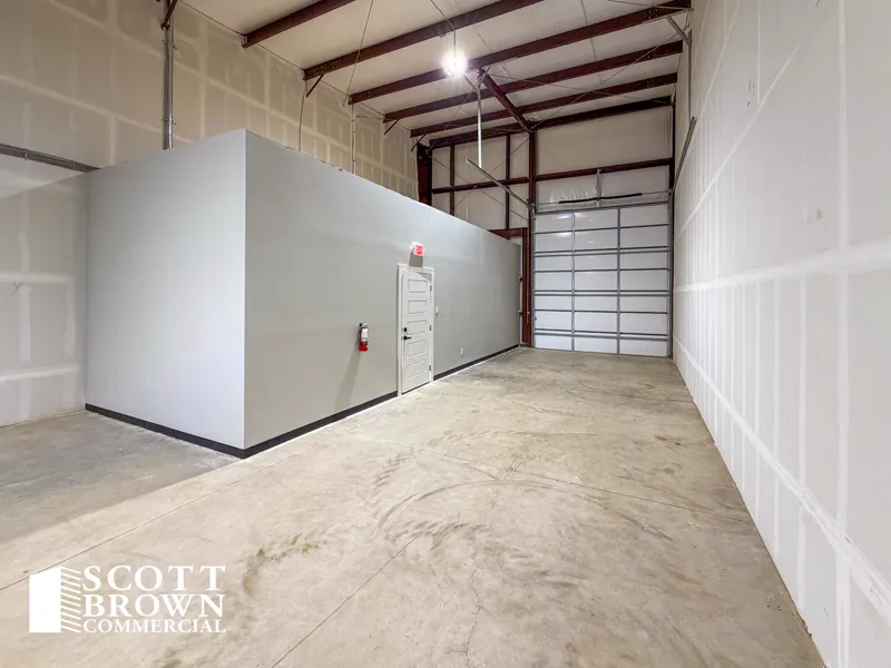 Inside a warehouse bay at Fusion Business Park, showing the back of the boxed-out office and restroom, red steel framing, white insulated walls, and a closed grade-level overhead door to one side.