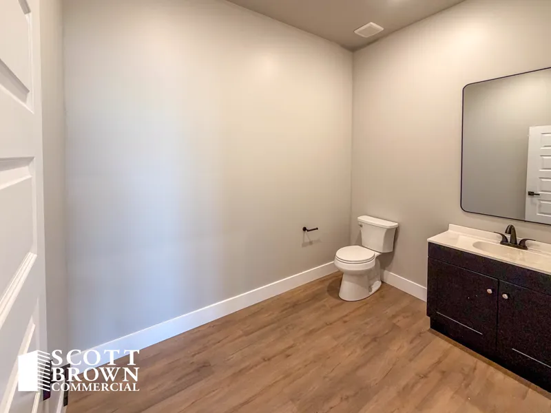 The private restroom in a Fusion Business Park suite, with a toilet, a dark vanity unit with a sink and mirror, and wood-effect plank flooring.